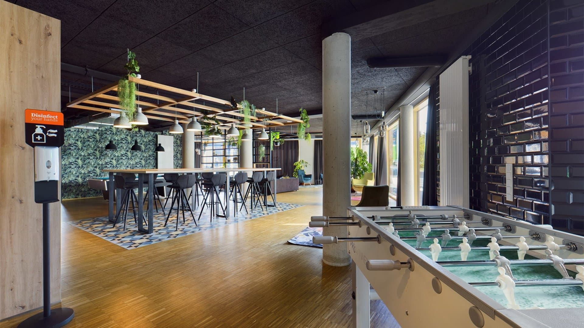 Moderner Gemeinschaftsraum mit Kickertisch, langen Tischen, Hockern und hängenden Pflanzen in Köln