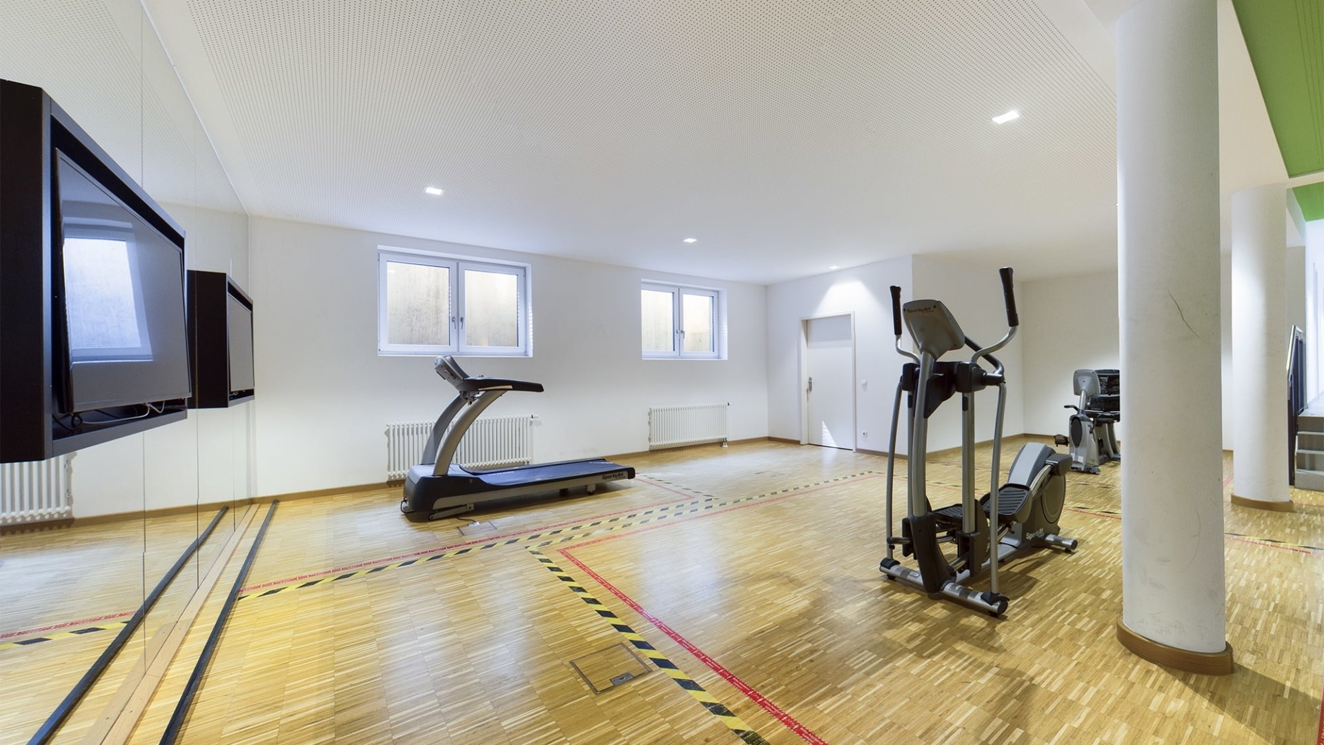 Fitnessraum mit Holzboden, zwei Trainingsgeräten und großen Fenstern in einer Wohnung in Mainz