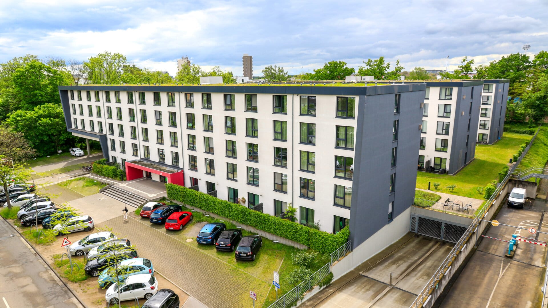 Modernes, mehrstöckiges Wohngebäude mit weißen Fassaden und roten Eingängen in Mainz, umgeben von Parkplätzen und Grünflächen