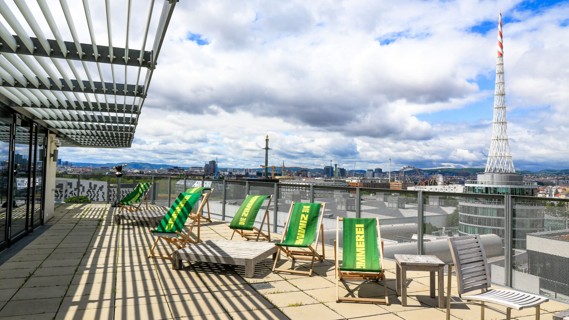 Dachterrasse mit grünen Liegestühlen und Blick auf Wiener Stadtpanorama mit Donauturm und Donau