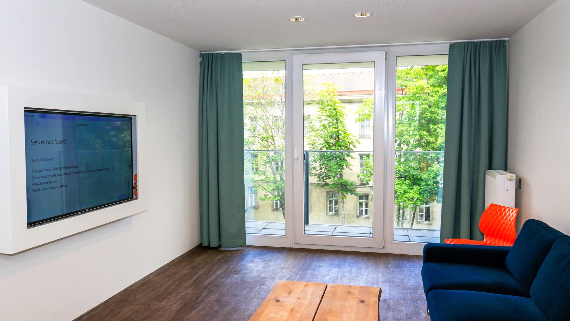 Wohnzimmer mit blauer Couch, Holztisch, großem Fenster mit Blick auf Bäume und Fernseher an der Wand mit Fehlermeldung