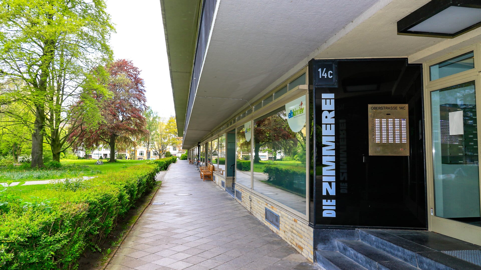 Eingang des Gebäudes Oberstrasse 14c mit Schild 'DIE ZIMMEREI' neben einem langen Gehweg und grünen Bäumen in Hamburg Grindel