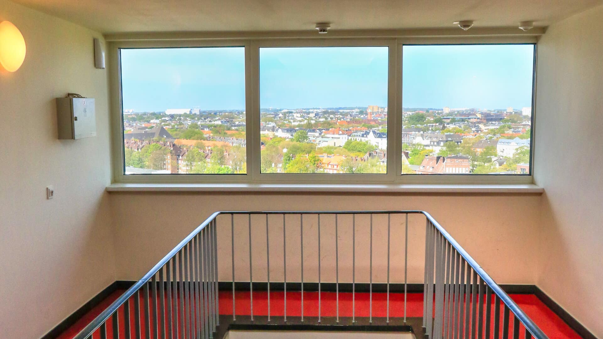 Treppenhaus mit rotem Teppich und großen Fenstern mit Blick auf die Stadt Hamburg