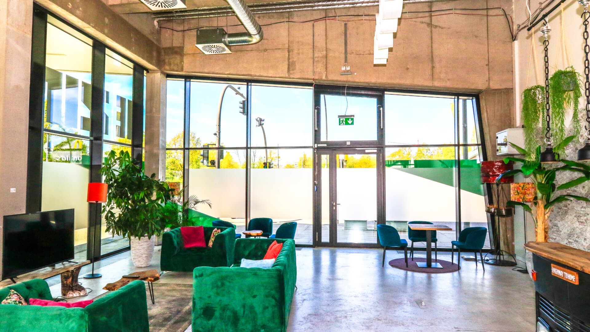 Lichtdurchfluteter Lounge-Bereich mit grünen Samtsofas, großen Fenstern und Pflanzen in einem modernen Industriegebäude
